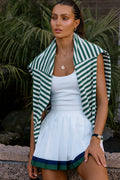 Woman wearing a green and white striped shrug over a white dress with plants in the background