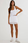 Woman wearing a white tennis outfit with a skirt on a plain background
