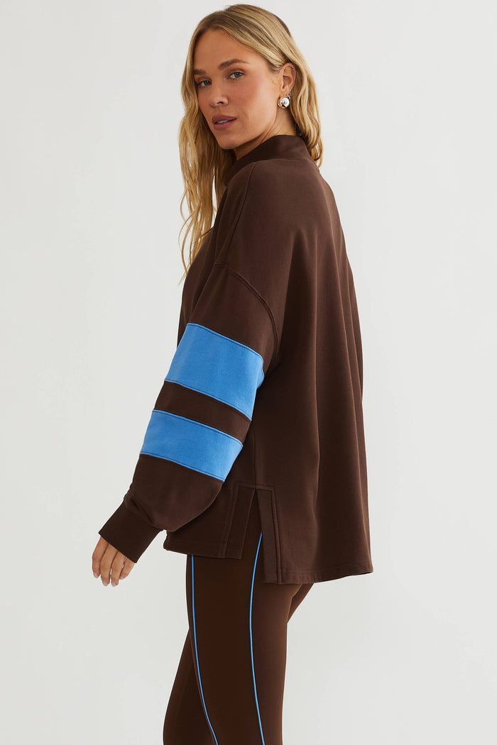 Woman wearing brown mock neck sweatshirt with blue color block on the sleeves.