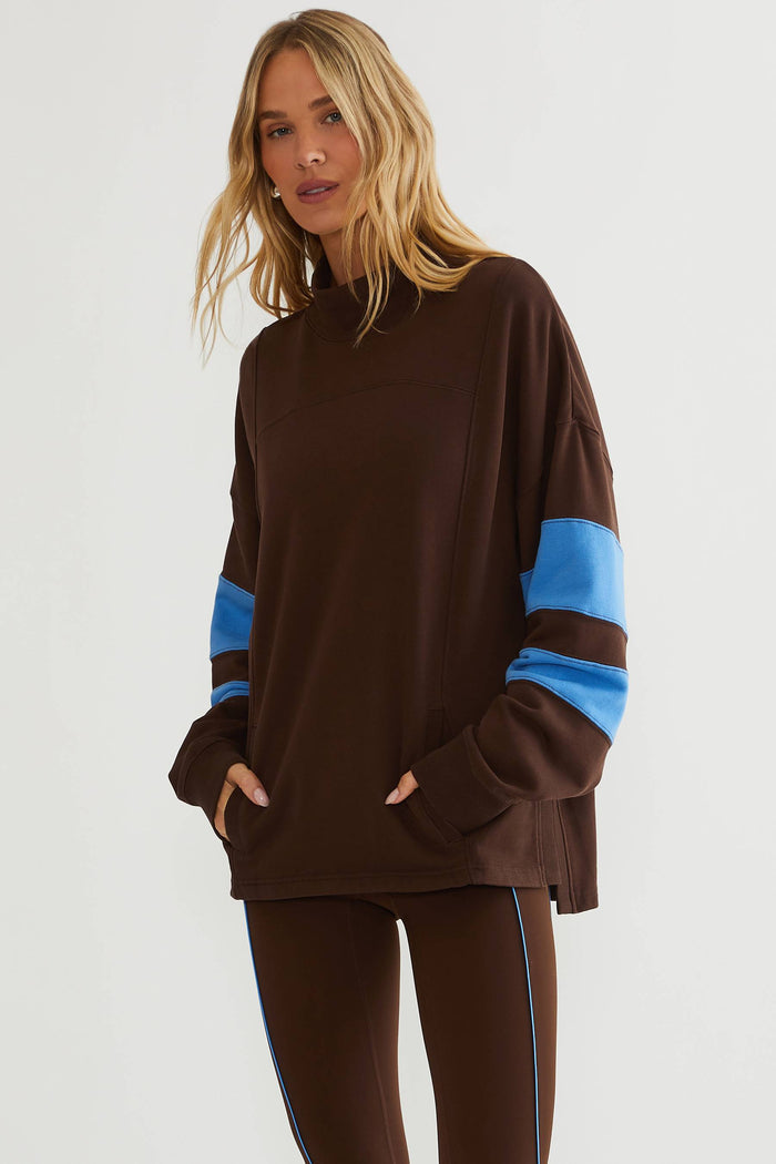 Woman wearing brown mock neck sweatshirt with blue color block on the sleeves.
