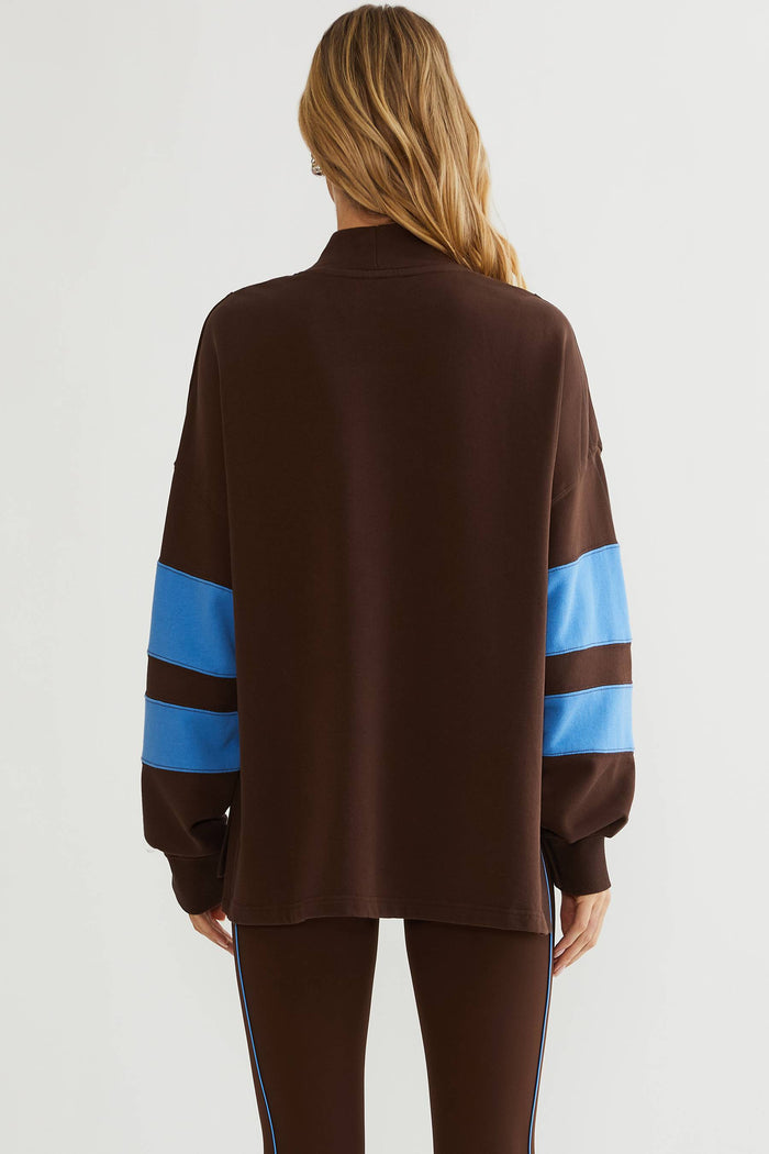 Woman wearing brown mock neck sweatshirt with blue color block on the sleeves.