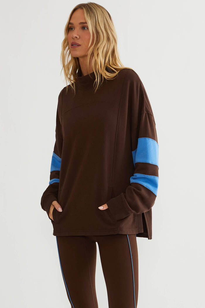 Woman wearing brown mock neck sweatshirt with blue color block on the sleeves.
