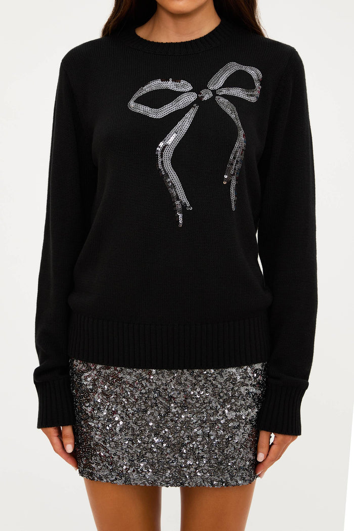 Black sweater with a bow design and silver sequin skirt on a white background