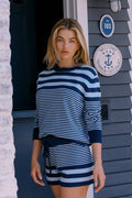 Woman wearing a blue and white striped outfit standing in front of a house with a plaque.