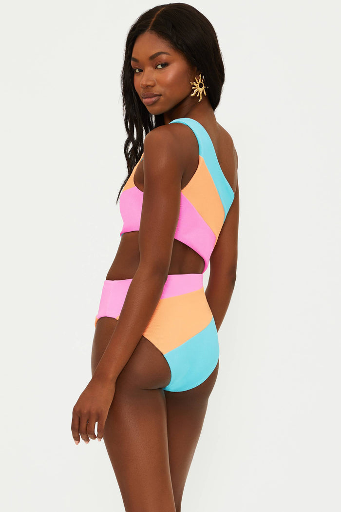 A model wearing an asymmetrical neckline, one-shoulder, colorblock patterned one-piece swimsuit in blue, orange, and pink.