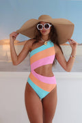 Woman wearing a colorful one-piece swimsuit and wide-brimmed hat on a beach.