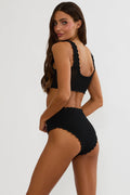 Woman wearing a black ribbed bikini set on a white background