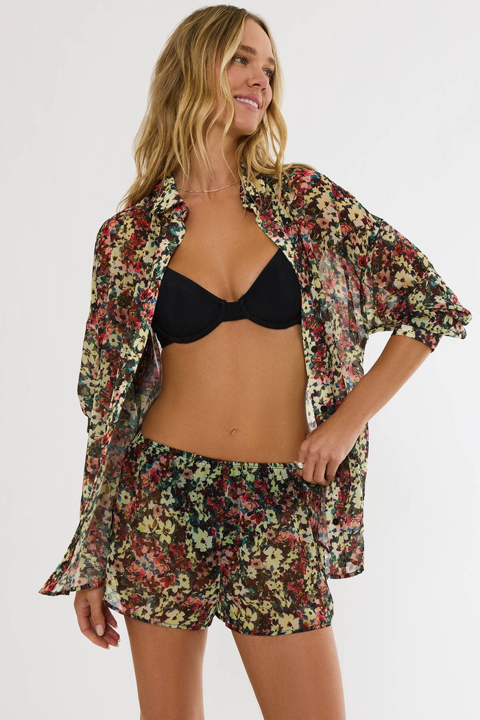Woman wearing a floral cover-up, black bikini top, and shorts on a white background