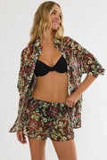Woman wearing a floral cover-up, black bikini top, and shorts on a white background