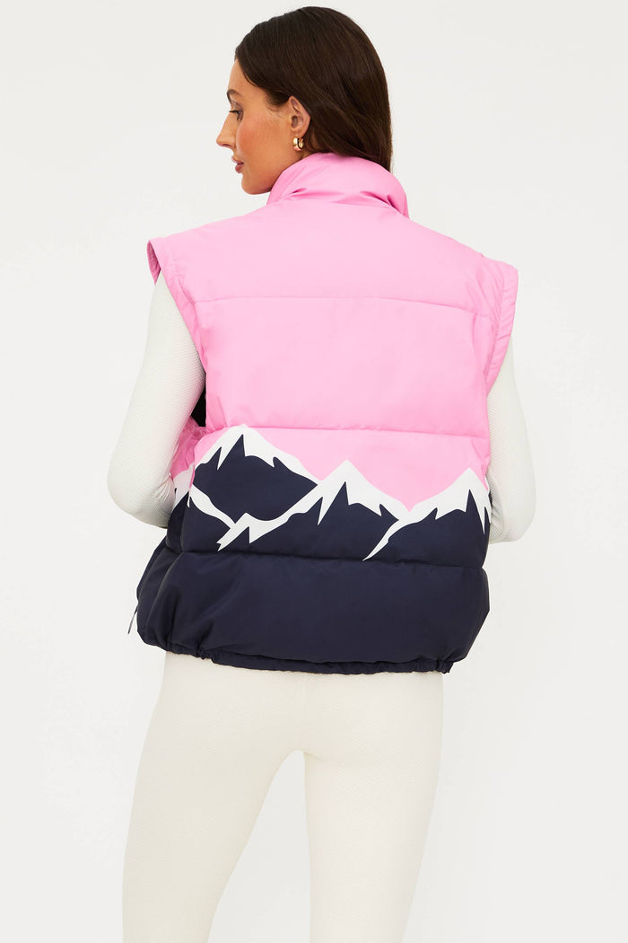 Person wearing a pink and navy puffer vest with mountain design on a white background