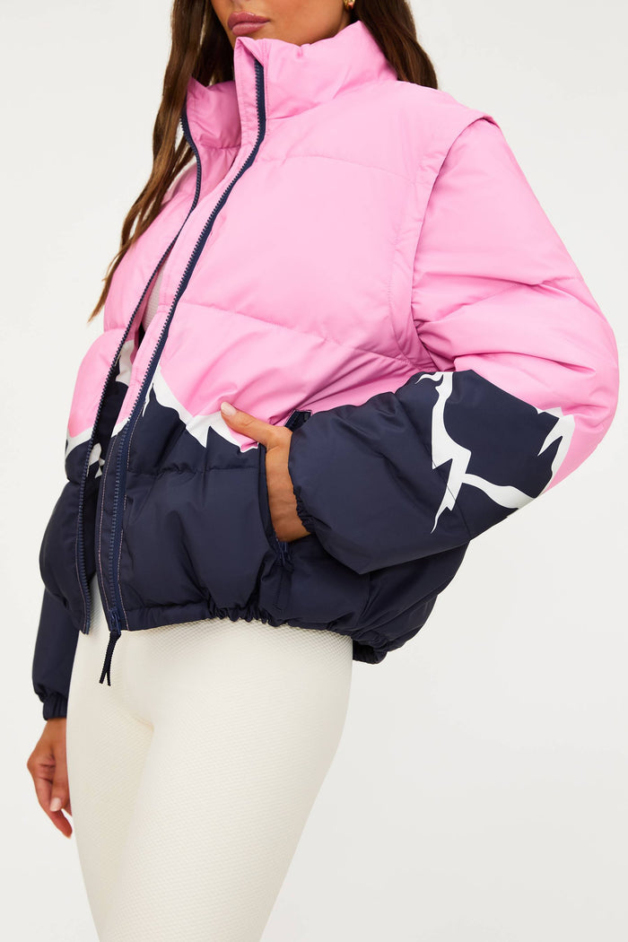 Pink and navy puffer jacket worn by a person on a white background