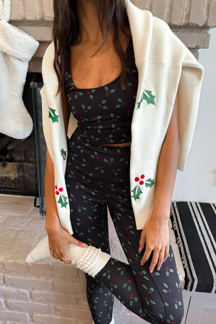 Woman wearing a black sports bra and leggings with green holly