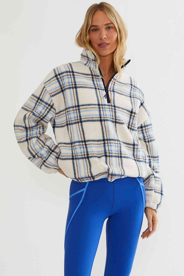Woman wearing cream, brown, and blue plaid sherpa quarter zip.