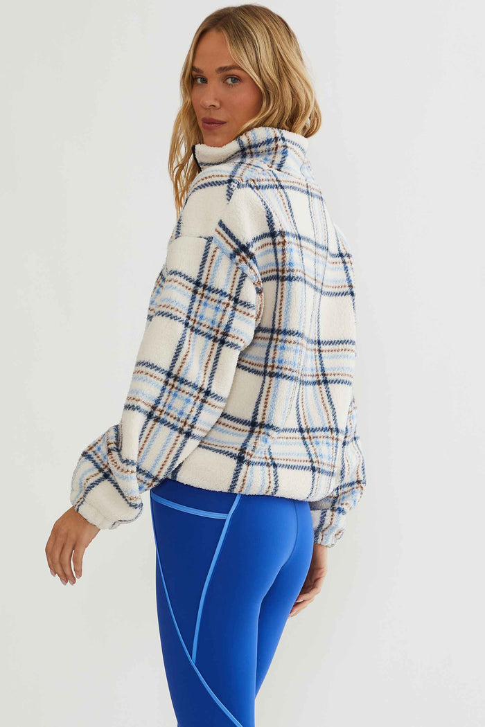 Woman wearing cream, brown, and blue plaid sherpa quarter zip.