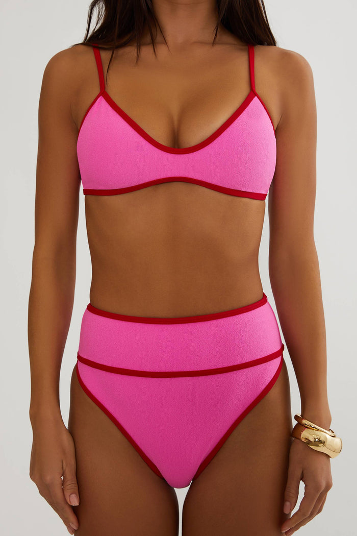 Pink bikini with red accents worn by a model on a plain background