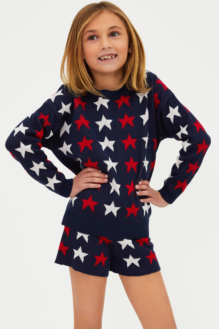 A child wearing a long sleeve navy blue sweater with a pattern of white and red stars.