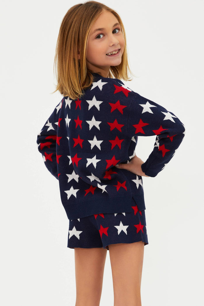 A child wearing a long sleeve navy blue sweater with a pattern of white and red stars.