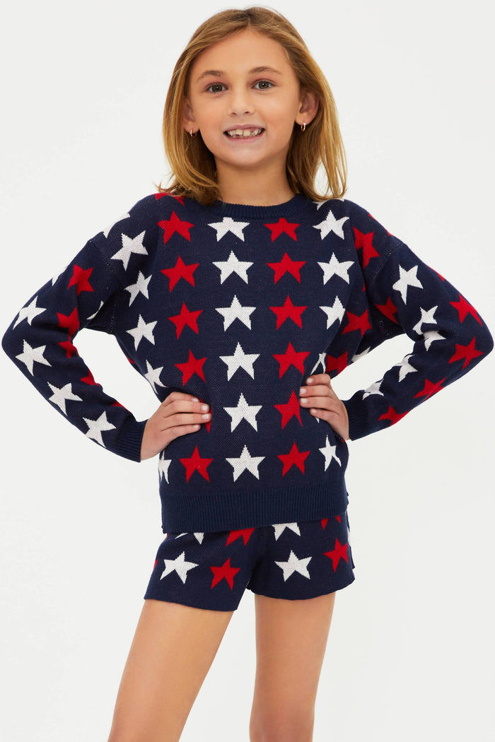 A child wearing a long sleeve navy blue sweater with a pattern of white and red stars.