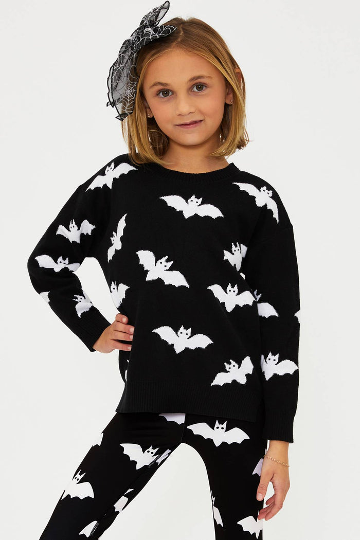 Child wearing a black sweater and pants with white bat patterns on a white background
