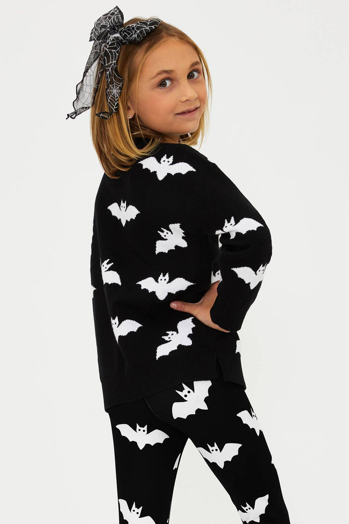 Child wearing a black outfit with white bat patterns on a plain background
