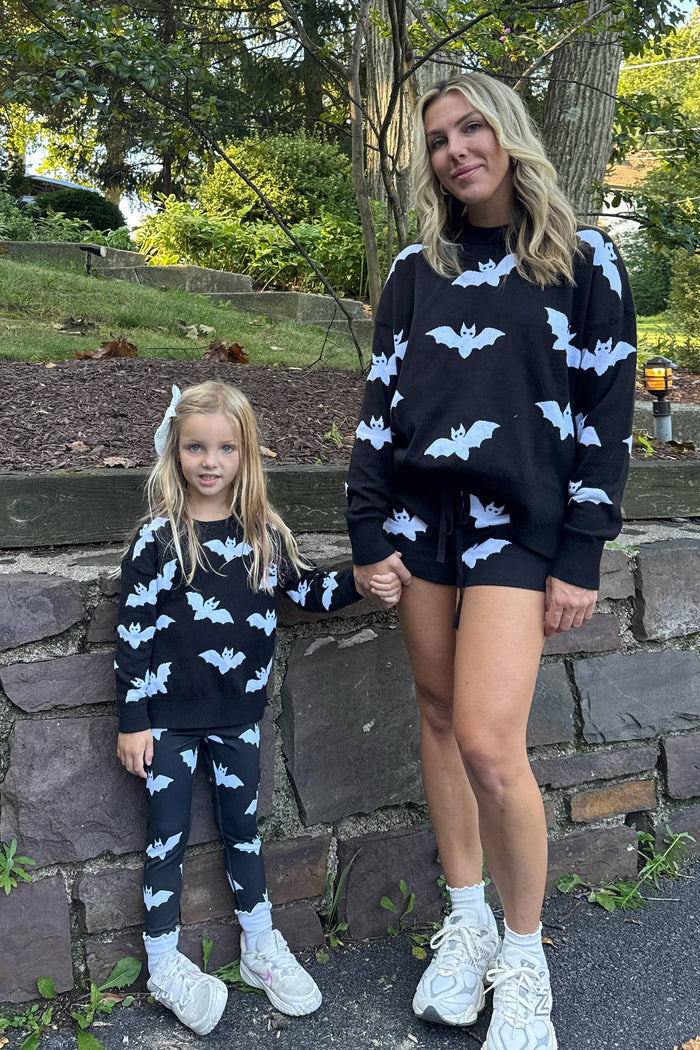 Woman and child wearing matching black outfits with white bat patterns outdoors.