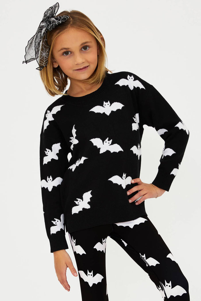 Child wearing a black outfit with white bat patterns on a plain background