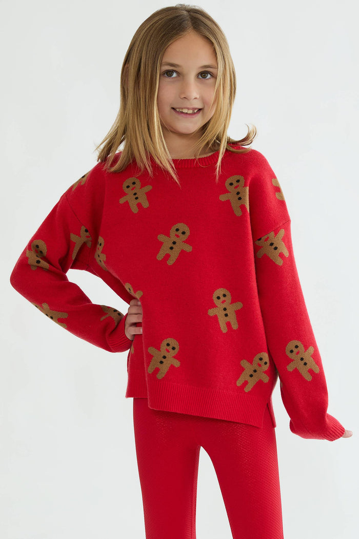Child wearing a red sweater with gingerbread man patterns on a white background