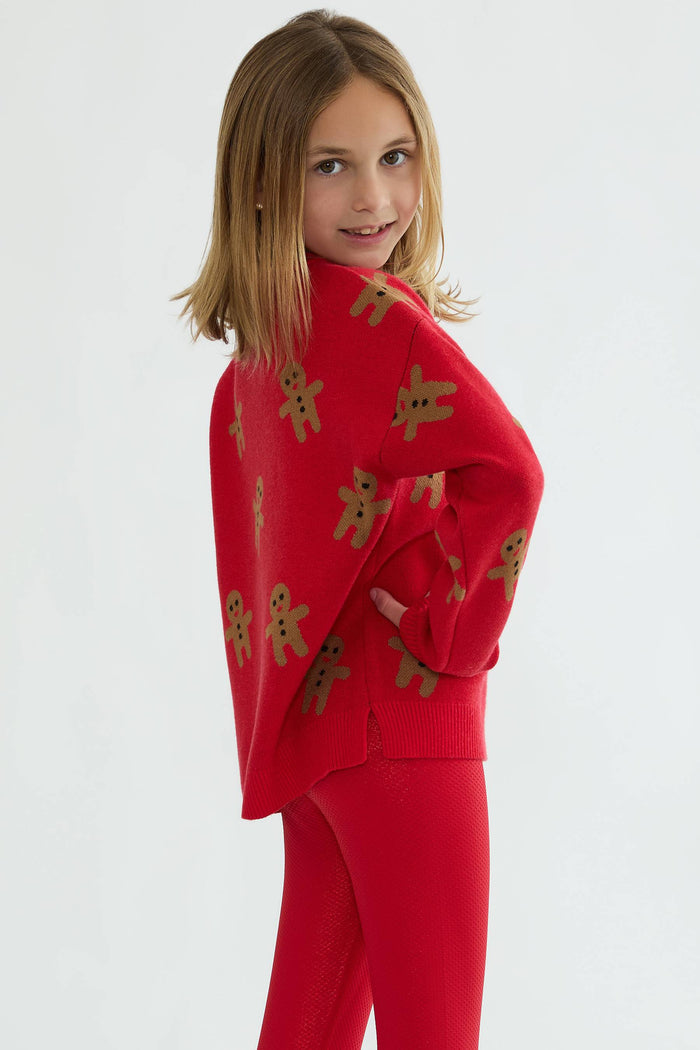 Child wearing a red outfit with gingerbread man patterns on a white background