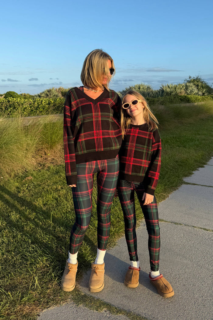 Two people wearing matching plaid outfits standing outdoors with a scenic background.