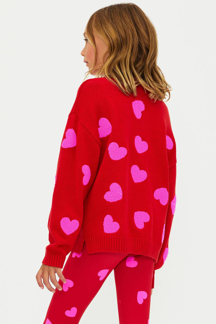 Person wearing a red sweater with pink heart patterns on a white background