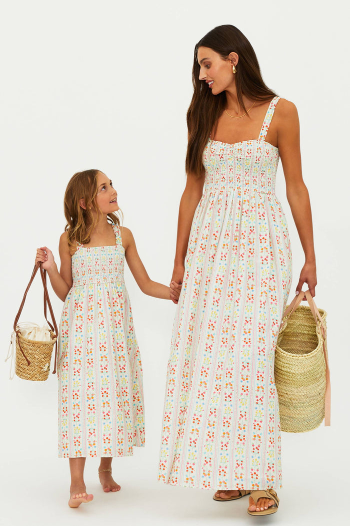 Woman and child wearing matching floral dresses holding hands against a white background