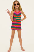A young girl posing in a colorful crochet swimsuit and matching cover-up skirt, with sunglasses, against a white background.