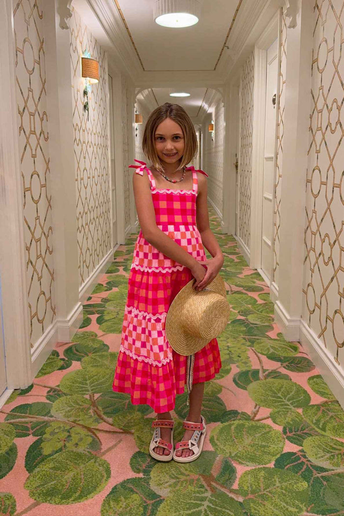 Young girl in a pink dress standing in a hallway with decorative wallpaper and green leaf-patterned carpet.