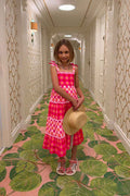 Young girl in a pink dress standing in a hallway with decorative wallpaper and green leaf-patterned carpet.