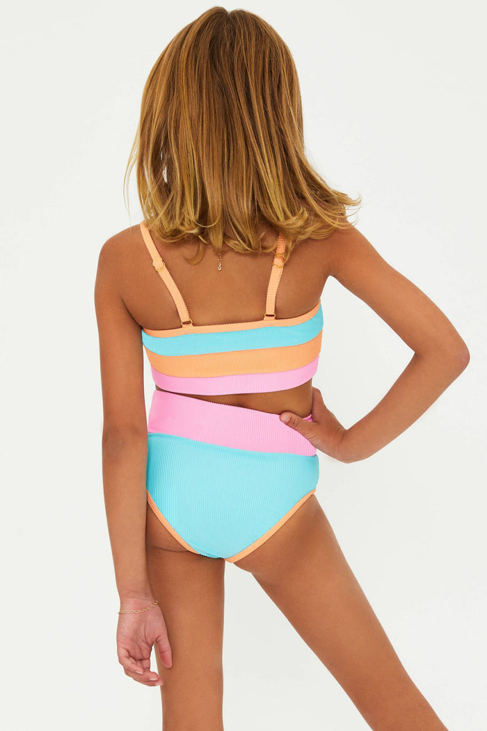 A child model wearing a two-piece swimsuit with horizontal color blocks in blue, pink, and orange, and white sunglasses