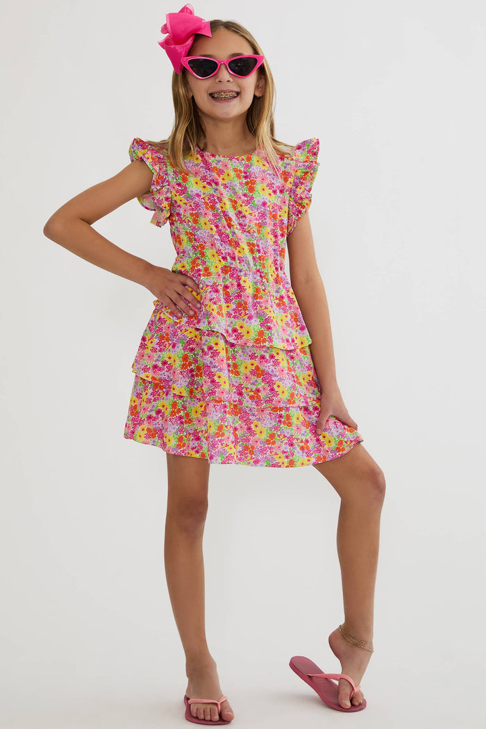 Young girl wearing a colorful floral dress with pink sunglasses and headband on a white background