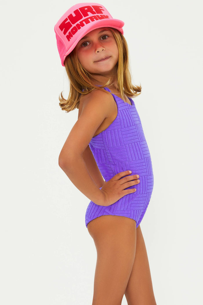 A child model wearing a purple one-piece swimsuit with a textured pattern and a pink hat
