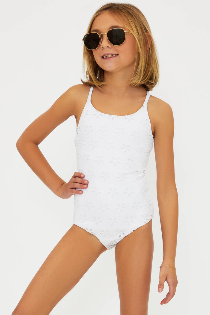 A girl wearing a white one-piece swimsuit with embroidered eyelet design and crossed back straps.