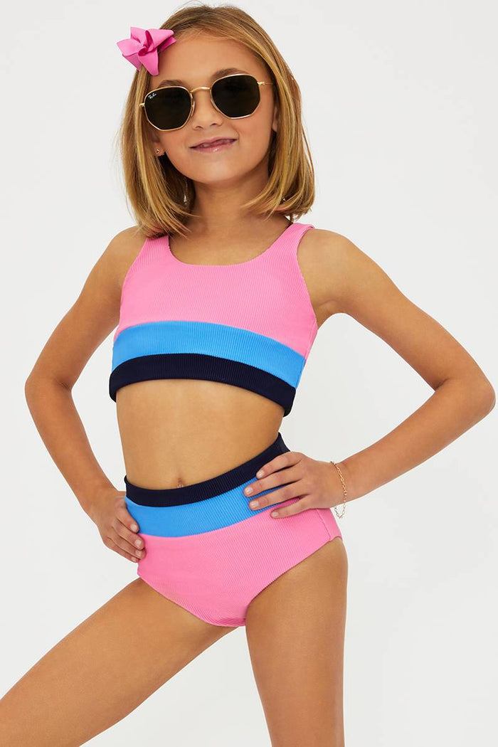 Young girl wearing a colorful two-piece swimsuit with sunglasses and a pink flower in her hair on a white background