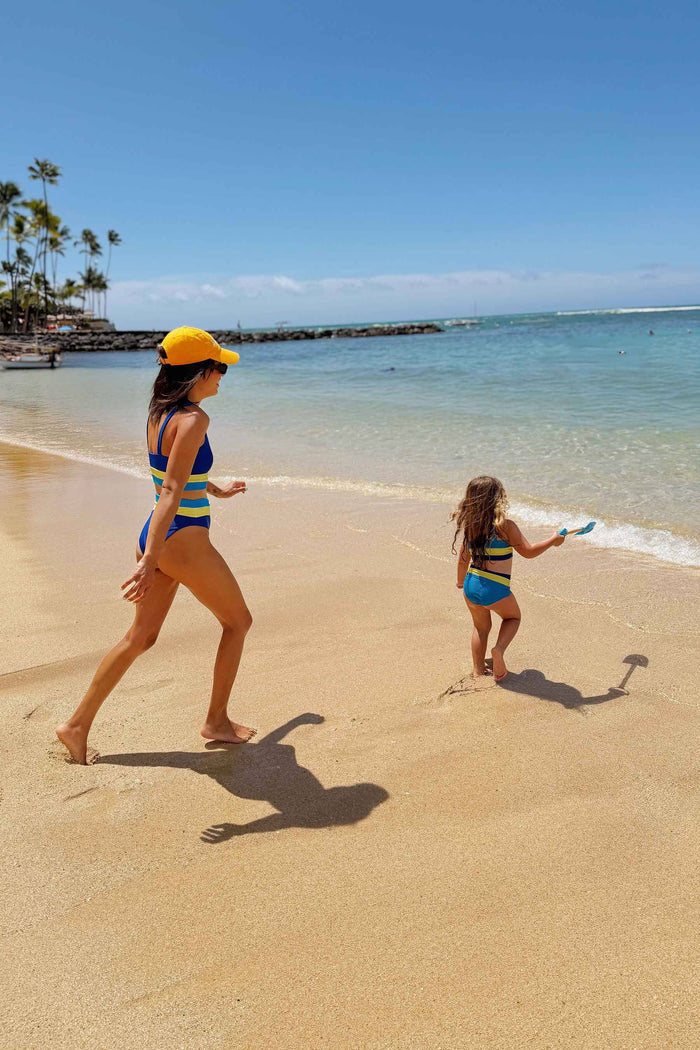 A child model wearing a two-piece swimsuit with a ribbed texture, featuring solid blue color with yellow and blue color blocks.