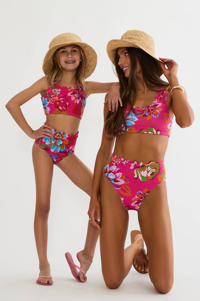Two women wearing matching floral swimsuits and straw hats on a white background