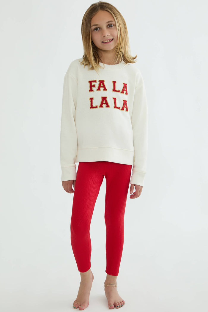 Young girl wearing a white sweater with 'FA LA LA LA' text and red leggings on a white background