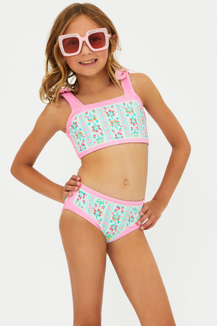 Young girl wearing a colorful bikini set with pink sunglasses on a white background