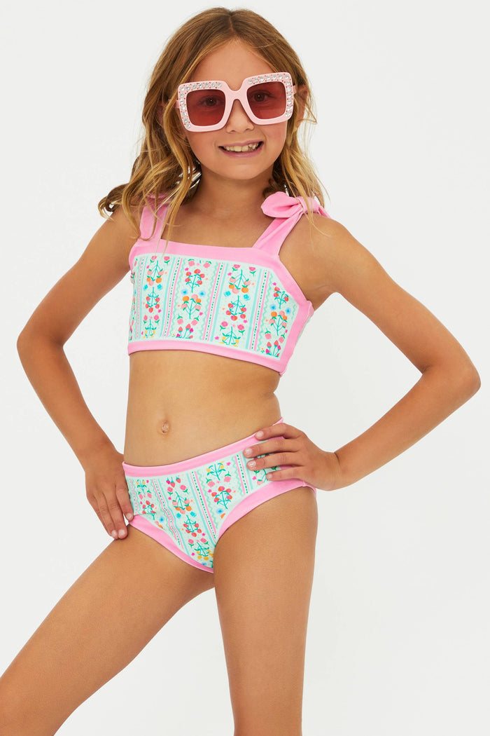 Young girl wearing a colorful two-piece swimsuit with pink accents on a white background