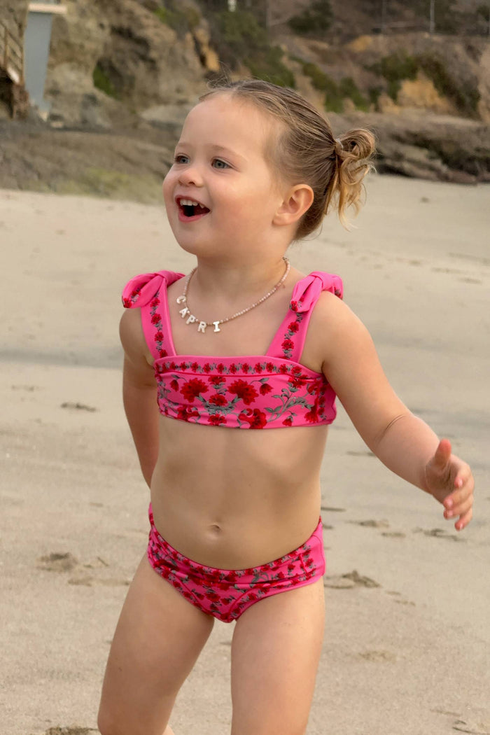 Young girl in a pink bikini standing on a sandy beach.