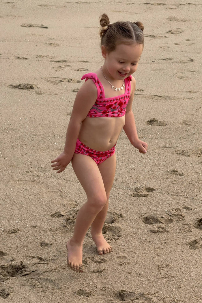 Young girl in a pink swimsuit walking on a sandy beach