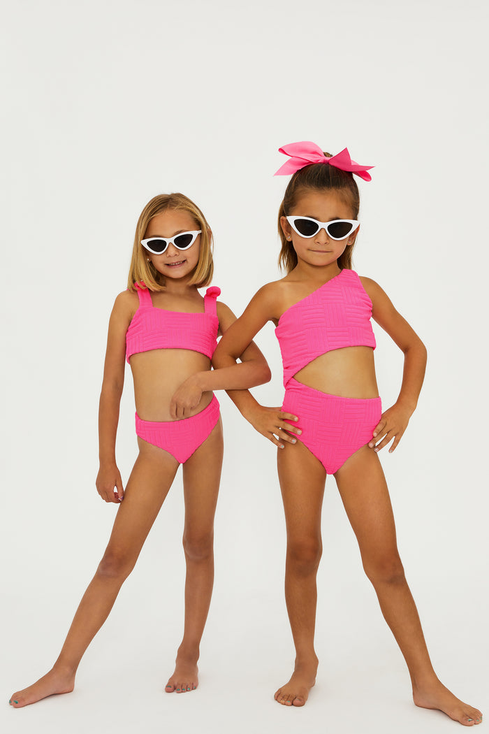 A young girl wearing a neon pink two-piece swimsuit with bows on the straps.