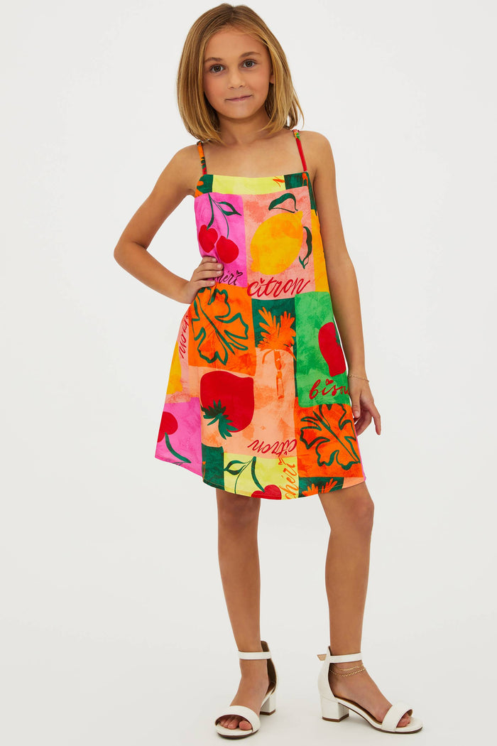 A young model wearing a sleeveless, multicolored floral dress with a square neckline and adjustable spaghetti straps.