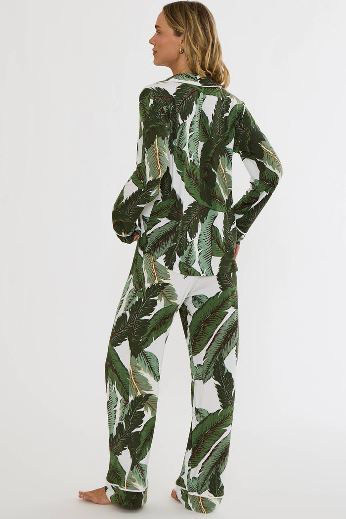 A woman modeling a matching two-piece pajama set with a green palm leaf print on a white background, shown from the back against a plain white studio backdrop.