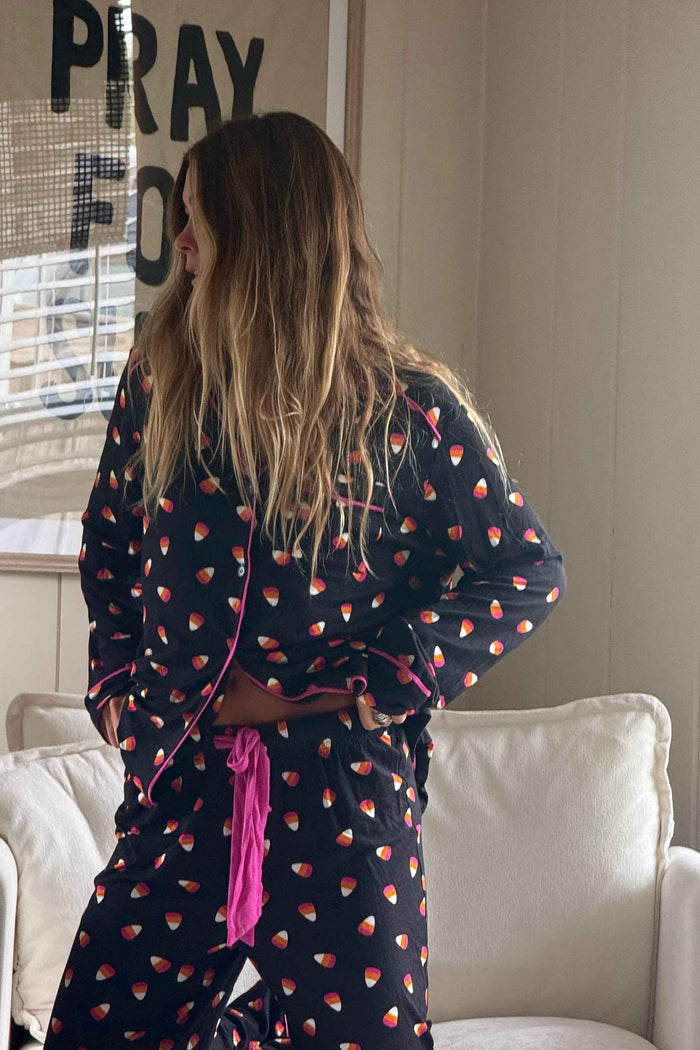 A woman wearing a black long-sleeve pajama set with a pink and orange candy corn pattern, standing in a living room setting.